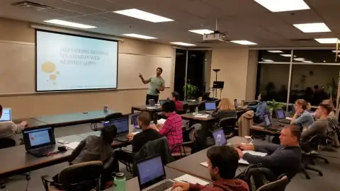 Class listening to an instructor near a whiteboard diagram